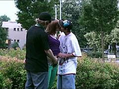 Два момка јебају младу плаву девојку у јавности док аутомобили и камиони гледају у овом групном сек видеу