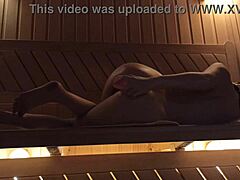 Eine junge Frau vergnügt sich in der Sauna mit einem rosa Dildo und erlebt einen Orgasmus